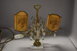 A vintage table lamp having lustre drops and twin candelabra style light fittings with paper