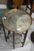 An early 20th century eastern stained mahogany and brass folding two tier table, the brass trays