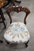 A Victorian mahogany nursing or low chair, having a carved and pierced top-rail over shaped supports