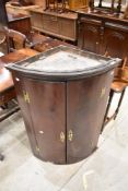 A George III mahogany bow-fronted corner cupboard, having brass H-form hinges, later brass