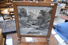 A mid 20th century oak firescreen, having printed material river-scene panel