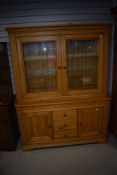 A modern golden oak bookcase or display case on having cupboards and three drawers to base (does