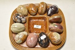 Twleve natural stone eggs, including marble and onyx, in brown glazed ceramic holder.