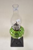 An antique oil lamp, having cast metal base and green glass reservoir.