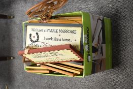 A box full of framed prints, plaques and similar, also included is a wicker carpet beater.