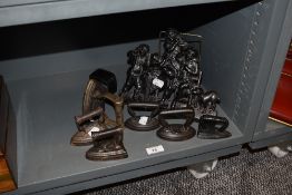 Six small cast iron stove top irons and a similar cast iron plaque.