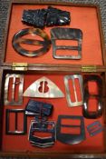 A wooden box containing an assortment of Art Deco buckles.