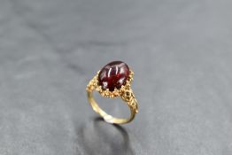 An oval red cabouchon stone ring having a decorative moulded claw set mount and shoulders to 9ct