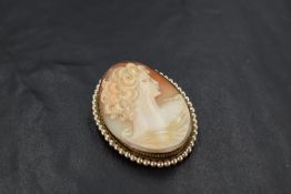 A conch shell cameo brooch depicting a maiden in profile within a pearl set silver mount