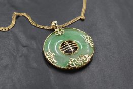 An Oriental style jadeite circular pendant in a yellow metal mount on a 9ct gold double link