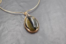 An oval tigers eye pendant in a 9ct gold collared mount on a 9ct gold wire and fixed chain, approx