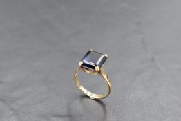 A 9ct gold and blue stone dress ring, the emerald-cut claw-set between shaped and pierced shoulders,