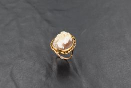 A conch shell cameo ring depicting a Bacchanalian maiden in profile in a collared mount on a