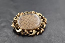 A yellow metal hair locket brooch having plaited hair panel within a decorative mount, no marks,