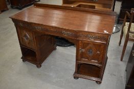 An early 20th Century oak desk, having Jacobean style cushioned panel doors and shaped carved