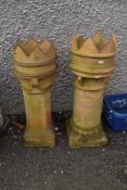 A pair of tall clay chimney pots with crown tops