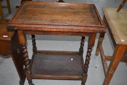 An early 20th century oak trolley table having fold over top, on twist frame
