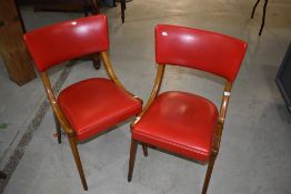 A pair of vintage chairs of stylised design having bent stained frames and vibrant red vinyl seats