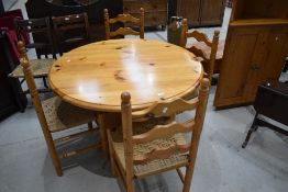 A vintage yellow pine circular kitchen table and set of four similar ladder back chairs with woven