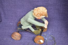 A early Steiff pull along and felt covered Boy wearing green jacket and pixie boots on metal cart