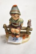 A small sized Goebel Hummel figure of boy sat on fence. Bearing a modern back stamp.
