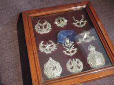 A small wooden and glazed display case containing 9 small Helmet plates or Cap Badges all to