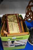 A box full of framed prints, plaques and similar. Also included is a wicker carpet beater.