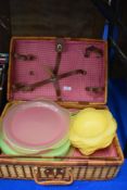 A traditional picnic basket housing a collection of plastic plates and bowl.