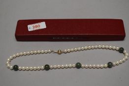 A pearl and green stone necklace, having numerous pearl beads interspersed by five green stone