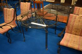 A glass topped table having wrought iron frame and set of four similar chairs with soft cushions