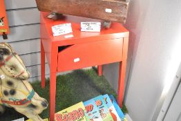 A modern red metal side table with drawer.