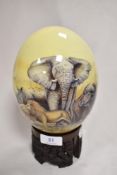 An Ostrich egg decorated with an African savannah scene of wild animals, with a carved wooden base.