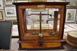 An antique cased set of apothecary or chemist balance scales in a glazed cabinet.