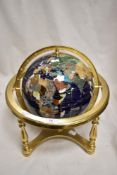 A modern globe made from semi precious stones and minerals on a yellow metal gimble frame.