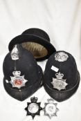 Two 20th century Police helmets with four badges including Cumbria Durham and Lincolnshire.