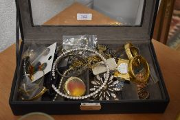 A case full of vintage costume jewellery including yellow metal bangles, a small clock and ear rings