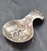 A George V silver caddy spoon, the bowl with embossed interior scene, the handle with foliate