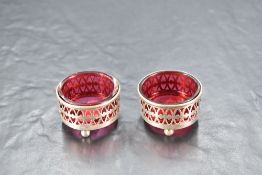 A pair of late Victorian silver and cranberry glass salts, of circular form with pierced decoration,