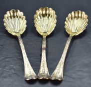 A group of three Victorian silver gilt serving spoons, the handles having scroll and shell terminals