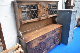 A Priory style oak dresser having glazed display section over triple drawer and cupboard base, width