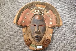 An early 20th century African Dan tribal ritual mask adorned with woven surround and sea shells