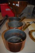 Three vintage copper kitchen pans with a large copper grain funnel.
