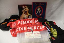 A lot of Freddie Mercury items with scarves and t-shirts and a badge and programmes with ticket
