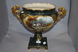 A late 19th/early 20th century two-handled urn, decorated with hunting scene vignette against a gilt
