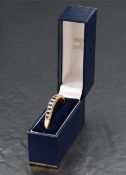 A 9ct gold hinged bangle having eleven graduated oval sapphires interspersed by twenty diamond chips