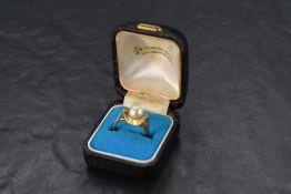 A cultured pearl ring having a single pearl in a stylised mount flanked by two small diamonds on a