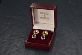 A pair of yellow metal stud earrings stamped 750 having a crescent shaped mount with facetted blue