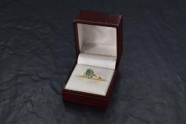 An oval emerald and diamond cluster ring in claw set mount with knife blade shoulders on an 18ct