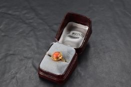 An 8ct gold ring having a circular coral cabochon set in a collared sunburst mount on a yellow metal