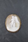A yellow metal mounted shell cameo brooch, of oval form, carved with the image of a winged